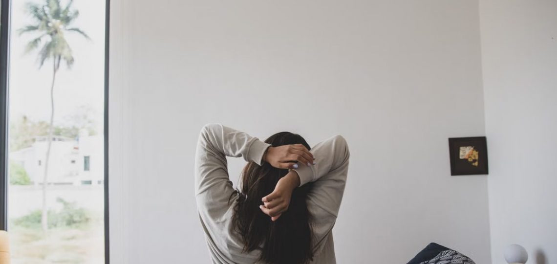A woman stretching in a modern bedroom with morning light, offering a sense of relaxation and tranquility.