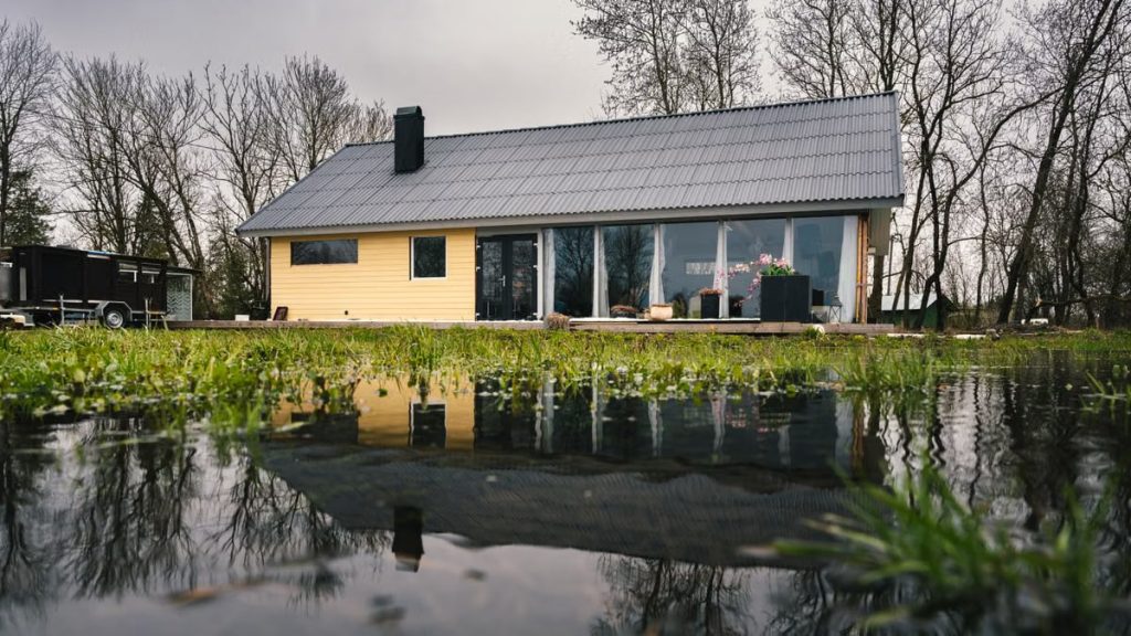 A picturesque rural house next to a reflecting pond surrounded by budding trees.